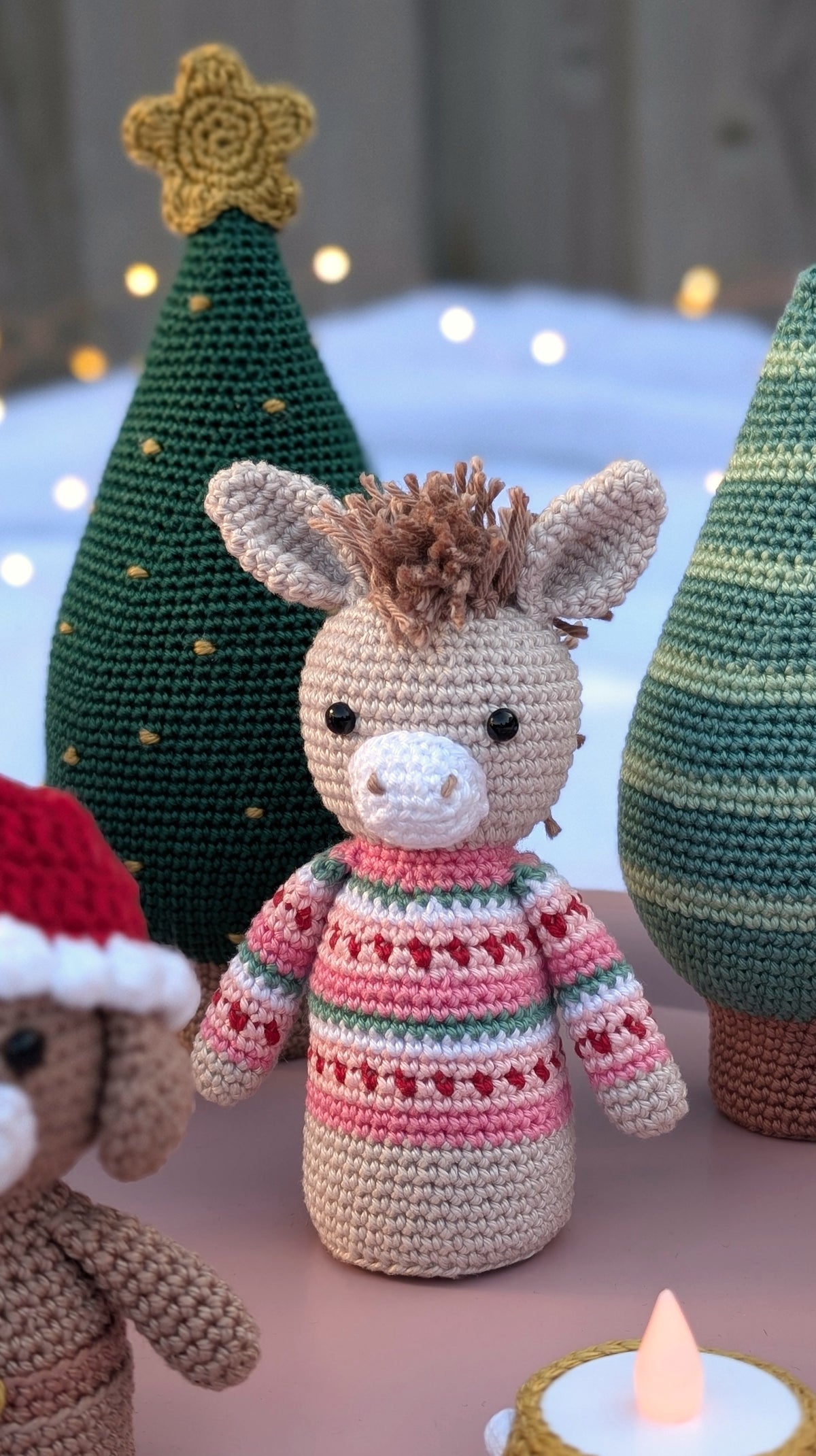 Gehaakte ezel uit de Wolplein x Mrs. Milly KerstCAL 2026 met kersttrui en kerstbomen op de achtergrond